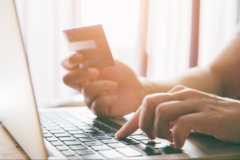 Kobieta pisząca na laptopie trzymająca w ręce kartę płatniczą