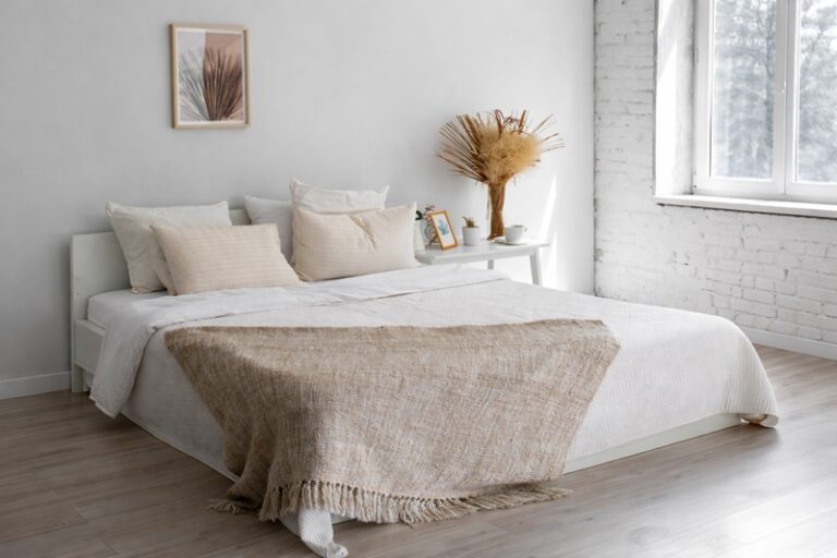 biała sypialnia z jasnym łóżkiem i naturalnymi dodatkami w spokojnej aranżacji