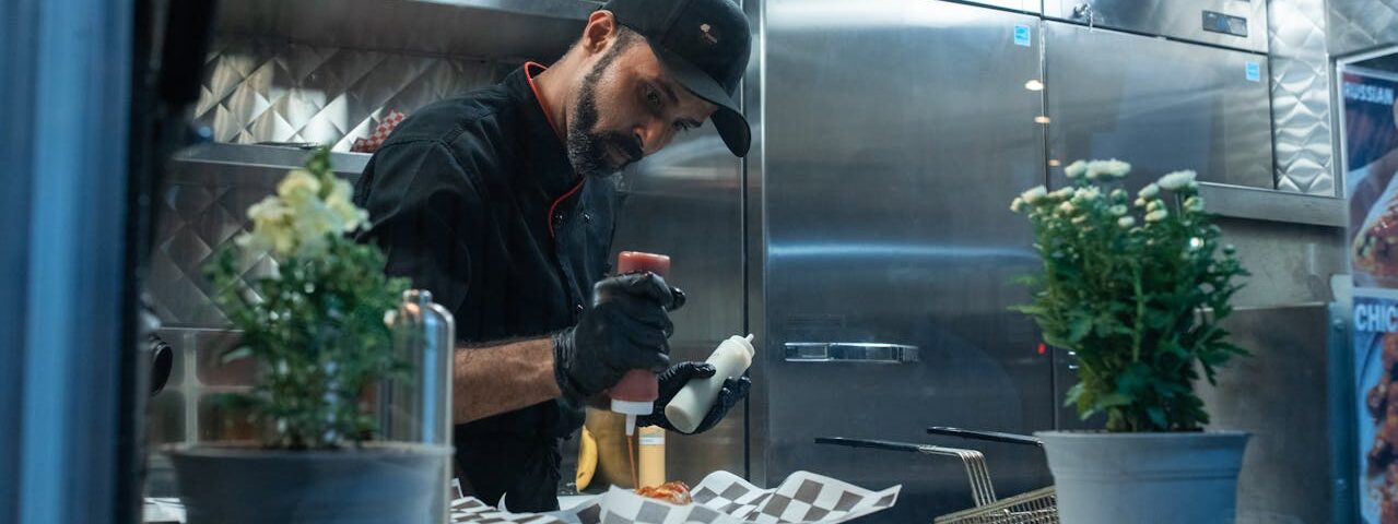 Kucharz przygotowujący danie street food w food trucku z egzotycznymi dodatkami